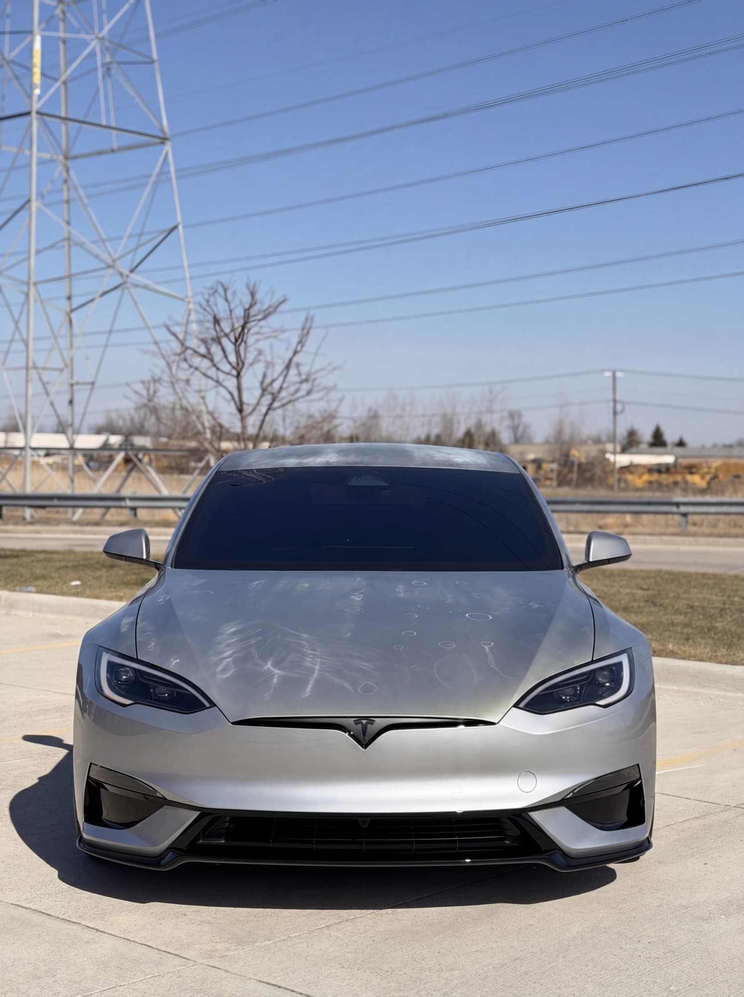 Same Silver Tesla Model S Plaid after three Detroit winters with no ceramic coating — visible spider-web swirl marks, dull paint, water-spot etching across the hood